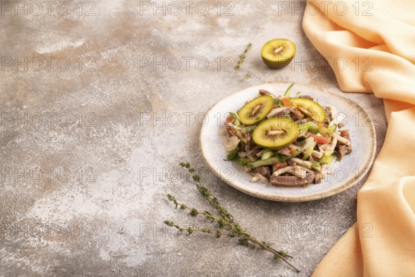 Meat salad with beef kiwi and vegetables on brown concrete background and orange linen textile.