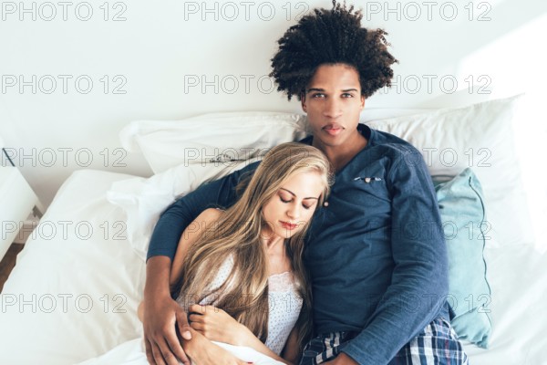 A serene moment between a couple lounging comfortably in bed. The woman rests her head on the man's