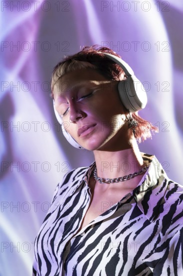 A young, trendy woman wearing headphones enjoys music. Her stylish zebra-print shirt and modern