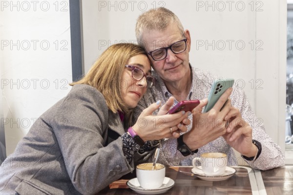 A couple with intellectual disabilities sits at a cafe table, with their smartphones. They share a