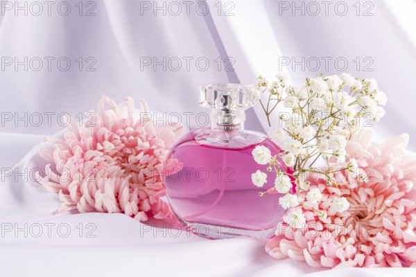 A stylish perfume bottle filled with pink liquid is elegantly nestled among pink flowers and white
