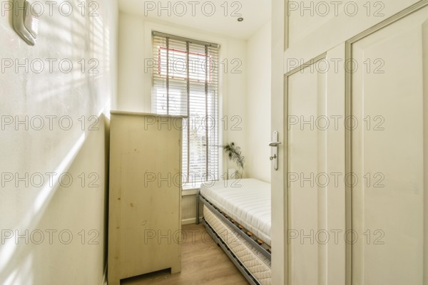 A bright and cozy room featuring a wooden cupboard and a neatly made bed, complemented by natural
