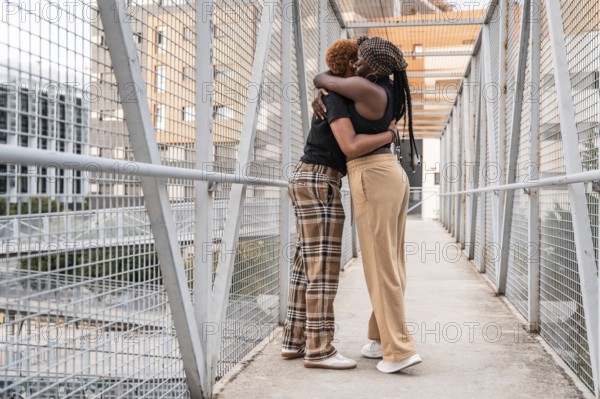 A loving LGBT multiethnic couple embraces on a metal bridge in an urban setting. Their warm hug