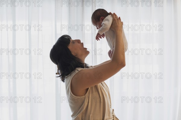 A joyful young mother holds her newborn baby lovingly in a softly lit room. This tender moment