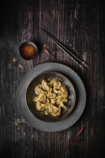 View from above of a plate of chili wontons on a wooden table next to chopsticks