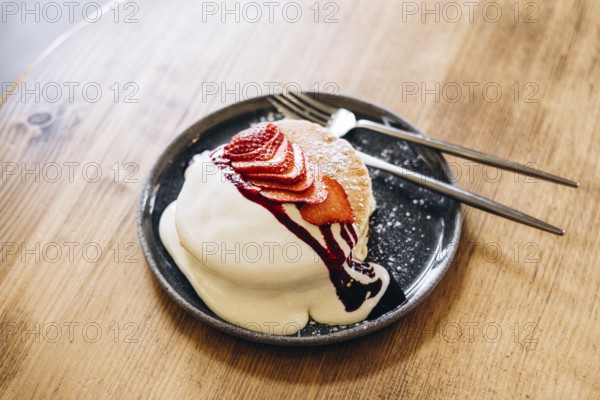 Fluffy japanese pancakes topped with fresh strawberries, a drizzle of cream, and berry sauce.
