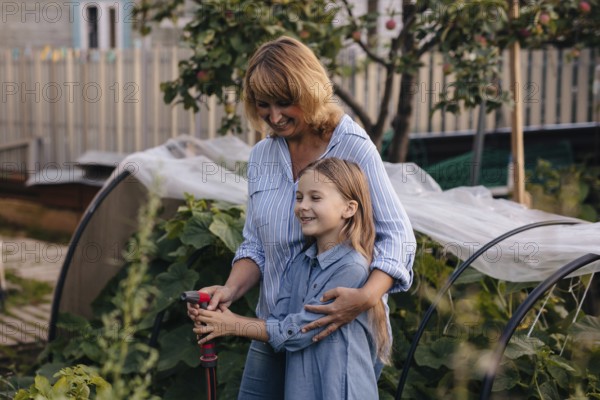 A joyful mother daughter duo tends to their greenhouse, surrounded by lush plants. They share a