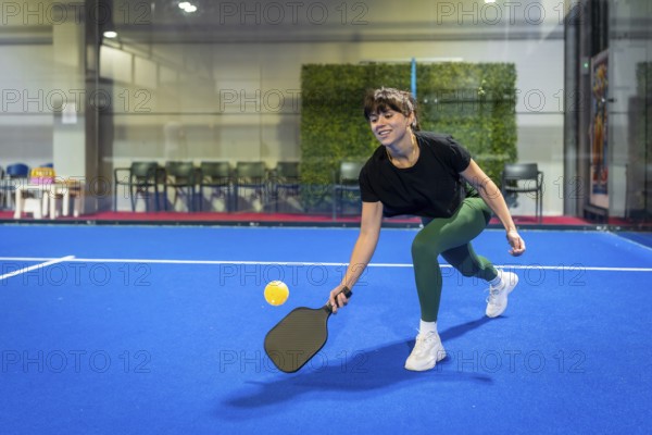 Woman playing pickleball on a vibrant blue indoor court, hitting the ball with her paddle during