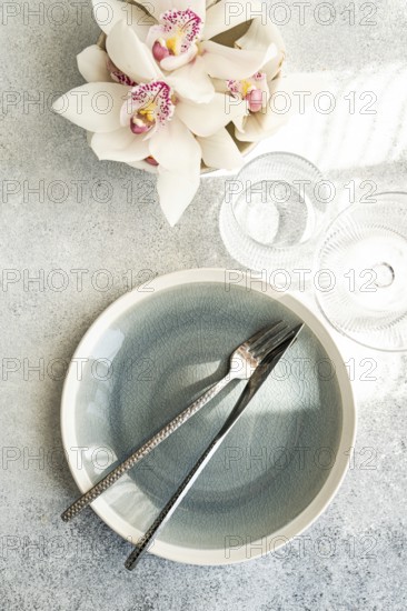 Stylish table setting features a textured ceramic plate, shiny cutlery, and delicate orchid flowers