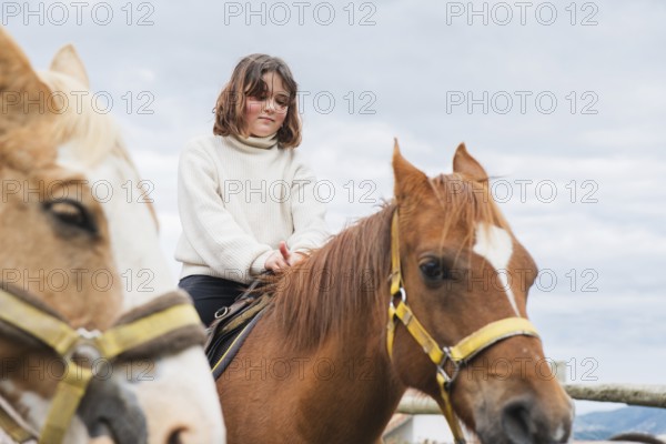 Young girl enjoying a peaceful day at the farm, sitting atop a horse. The clear sky and gentle