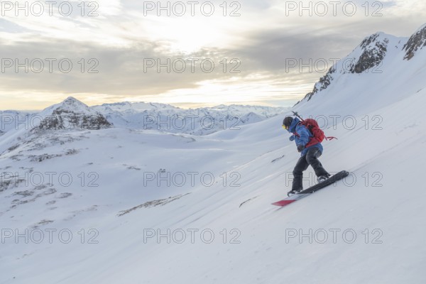A snowboarder rides down a pristine snowy slope, surrounded by stunning alpine peaks under a soft,
