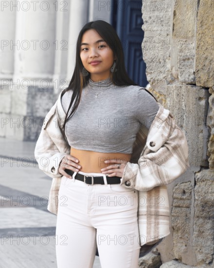 A young woman poses confidently in a chic urban setting, wearing a trendy plaid jacket over a gray