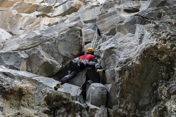 A climber in a red shirt and helmet is scaling a rugged mountain face. The image captures the
