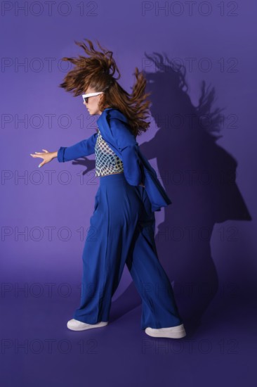 A young woman dances energetically against a vibrant purple background. Her dynamic pose and