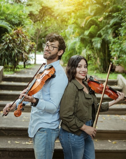 Portrait of two young violists back to back outdoors. Portrait of smiling male and female violinist