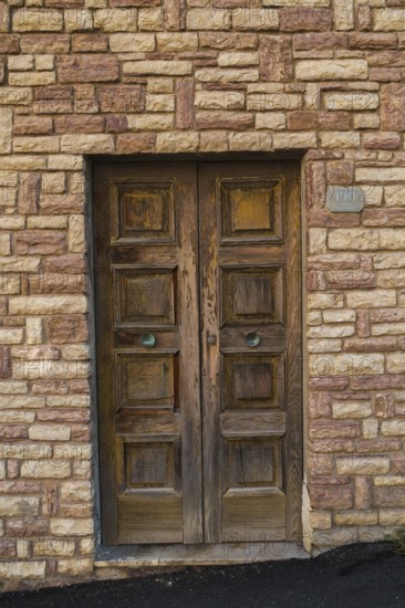 Distressed brown painted wooden entrance door on tan and beige cut stone residential building