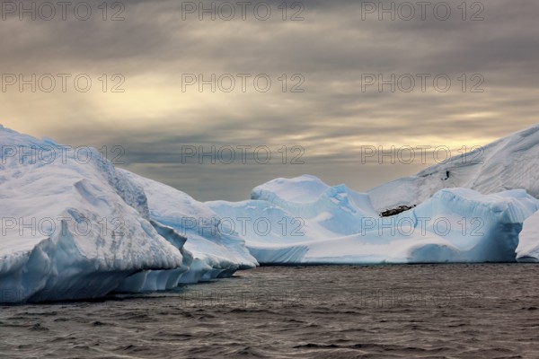 Huge, sharp icebergs stretch out under a cloudy sky as dusk falls, icebergs in the landscape of the