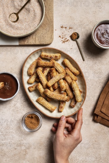 Top view of cropped unrecognizable hand holding a ceramic plate filled with sugar-coated churros,