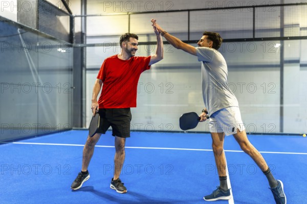 Male pickleball players celebrating victory and sportsmanship, high fiving on an indoor court after