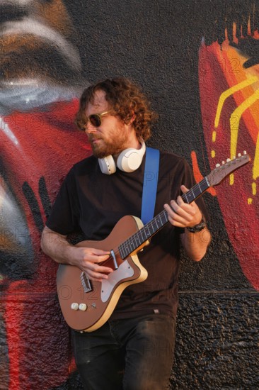 Hipster street musician in black playing electric guitar in the street on sunset leaning on a