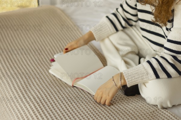 A person in a cozy, striped sweater sits cross-legged on a bed with a textured blanket, holding an