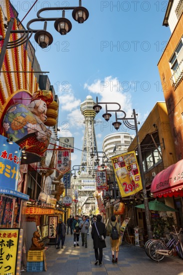 Lots of colorful signs in a pedestrian zone with shops and restaurants, behind Tsutenkaku Tower,