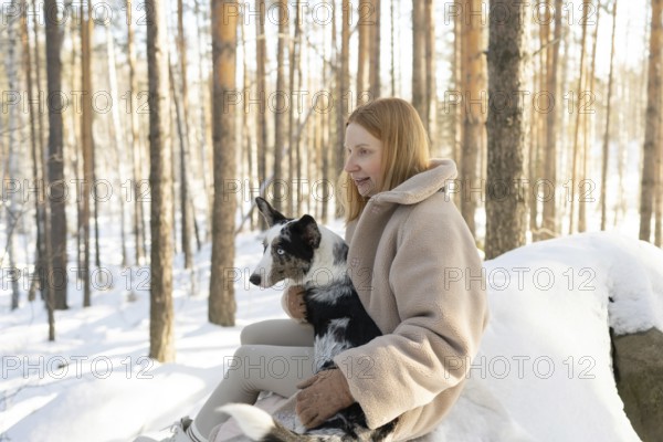 A redhead woman walks through a snowy forest with her Border Collie. The serene winter scenery