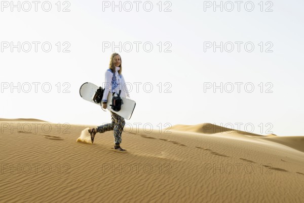 Young woman with snowboard in the sand dunes, near Merzouga, Meknès-Tafilalet region, Erg Chebbi,