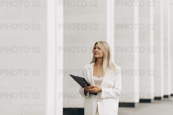 A professional woman holding a folder walks confidently beside a modern architectural structure.