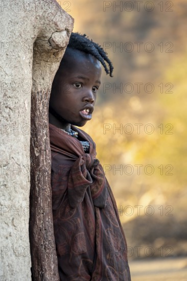 Himba girl leaning against a traditional mud hut, in the morning, traditional Himba village,