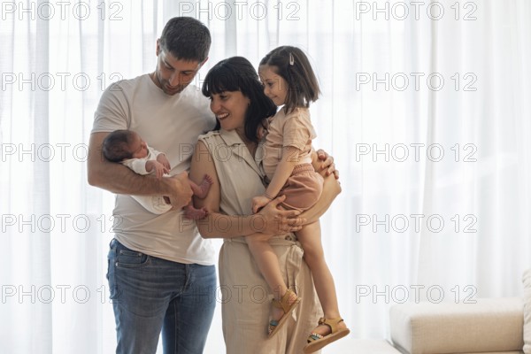 A joyful young family is gathered indoors, celebrating the arrival of their newborn baby. The big