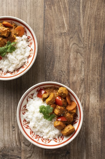 From above, two bowls of Hungarian pork goulash served with rice, garnished with a parsley leaf on