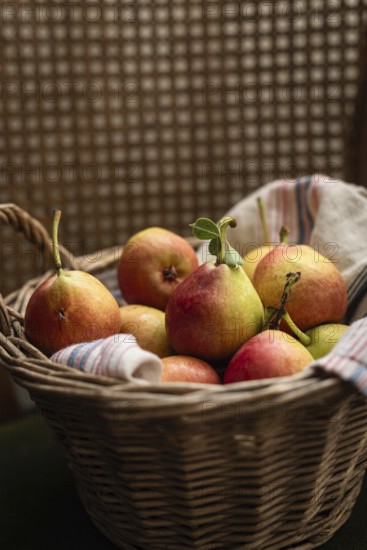 A charming wicker basket filled with ripe pears, resting on a striped textile. The warm tones and