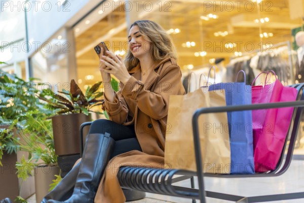 Happy woman taking a break from shopping at the mall, sitting on a bench with shopping bags and