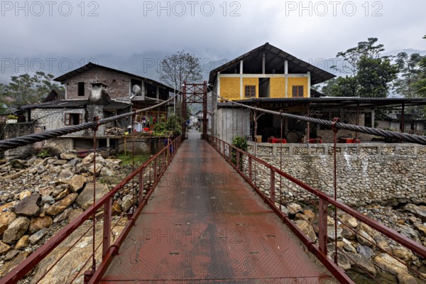 A metal bridge connects two older buildings, one of them yellow, under a grey cloudy sky, A bridge