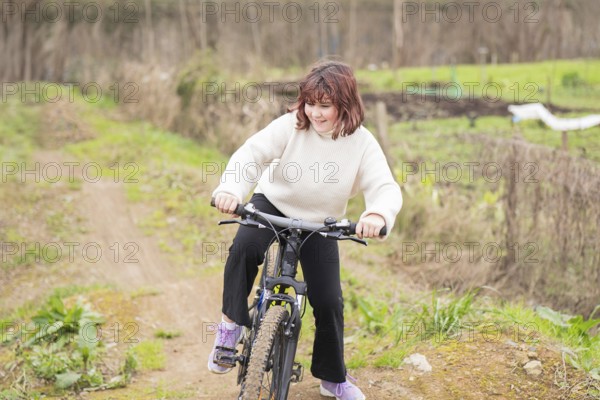 A young girl enjoys biking on a dirt trail, surrounded by greenery. She wears a cozy sweater and