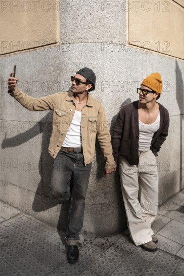 A Colombian couple taking a selfie, hand in hand. They lean against a city wall, embodying modern