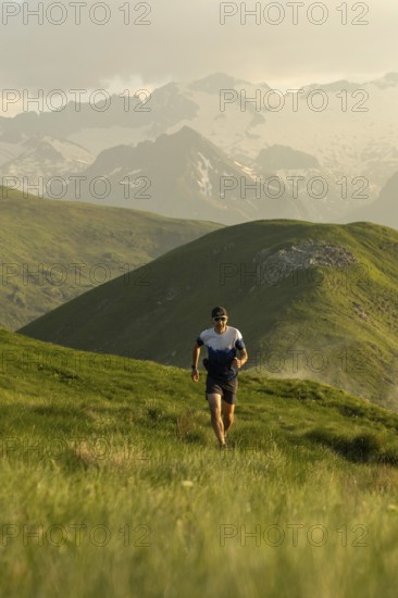A lone runner navigates a picturesque trail through vibrant green mountains, wearing a hat and