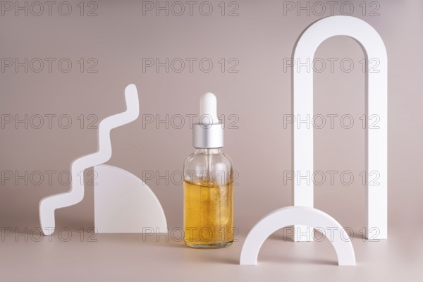 A modern cosmetic serum bottle with a silver dropper surrounded by minimalist geometric shapes on a