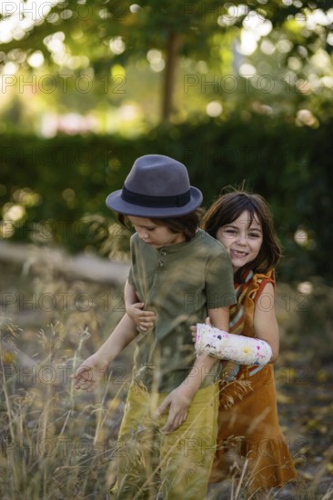 Two children playfully enjoy a sunny day outdoors. One wears a hat, while the other has a colorful