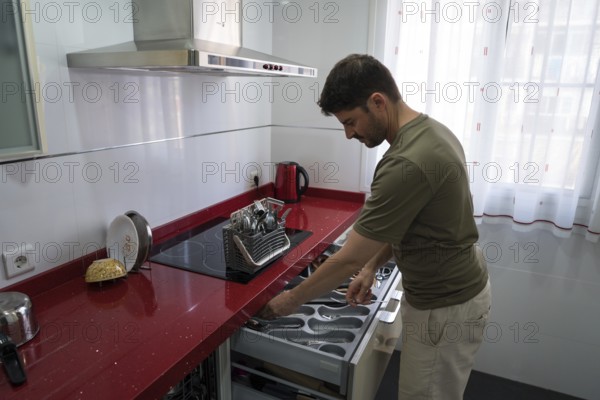 A man is organizing utensils in a modern kitchen. He carefully arranges cutlery in a drawer,