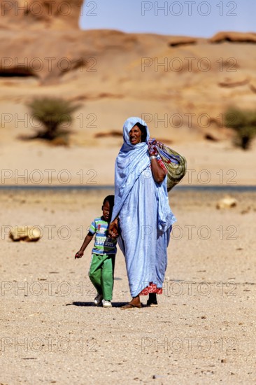 Mother and child in traditional dress walk together through a barren, sandy desert, woman in the