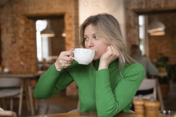 Woman enjoys a relaxing morning at a cozy cafe, sipping coffee. The warm interior ambiance adds to