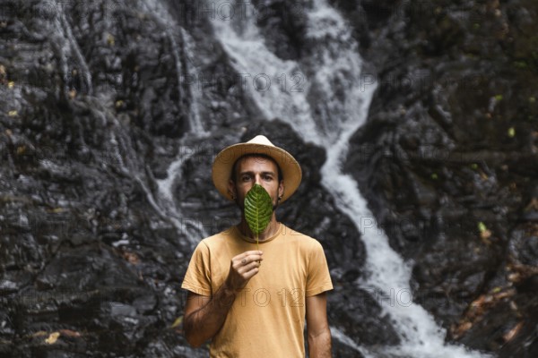 Man from Spain holding a leaf in front of his face, with a waterfall in the Choco Andino