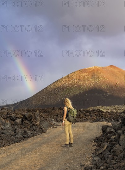 A woman with a backpack stands on a rocky path in Timanfaya National Park, Lanzarote. A vibrant