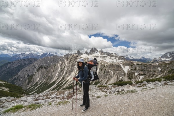 A smiling mother with her baby in a carrier hikes through the breathtaking snow-capped peaks of Tre