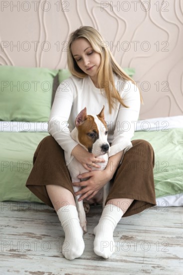 A woman sits comfortably in a home setting, gently holding and looking at a young dog in her arms.