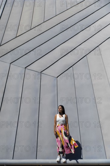 A woman in a vibrant, colorful outfit stands against a backdrop of sleek, modern architecture. Her