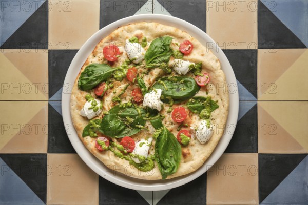 Top view of a delicious pizza with pesto, cherry tomatoes, basil and stracciatella cheese, served