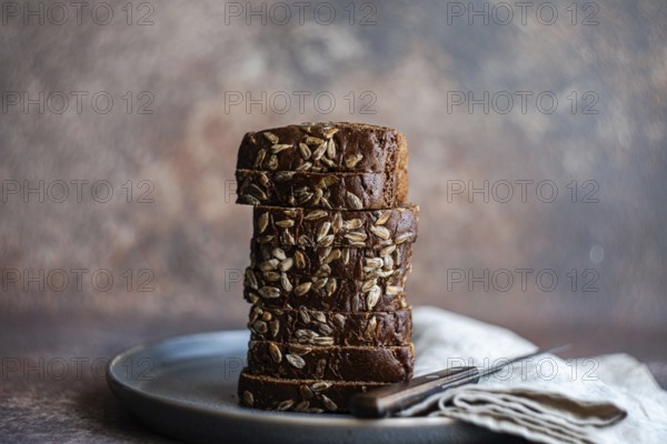 A stack of freshly sliced whole wheat bread with seeds sits artfully arranged on a ceramic plate.